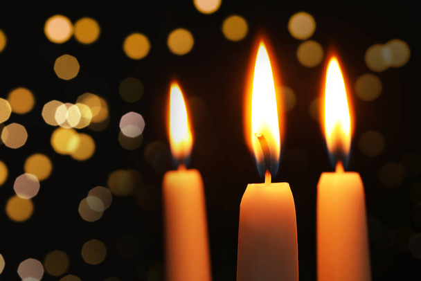 Burning candles on dark background with blurred lights, closeup. Bokeh effect - Photo, image