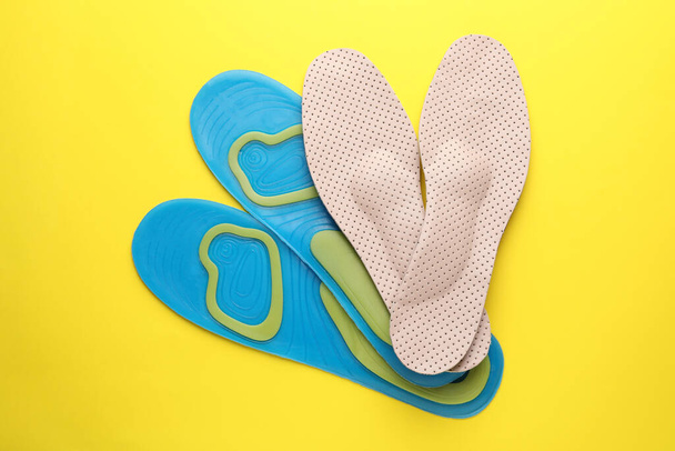 LIght blue and beige orthopedic insoles on yellow background, flat lay - Фото, изображение