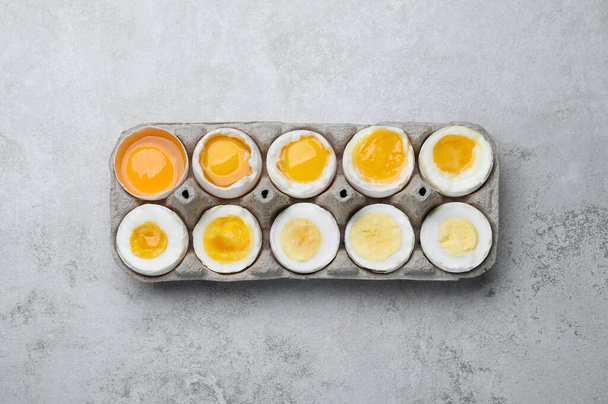 Boiled chicken eggs of different readiness stages in carton on light grey table, top view - Fotó, kép