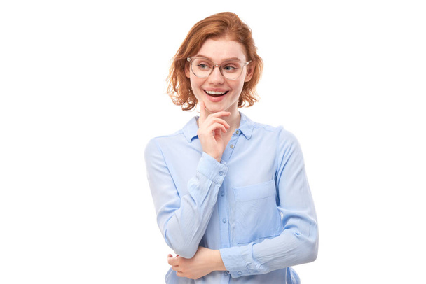 Smart redhead girl in glasses and business shirt holding chin thinks doubts, makes decision isolated on white studio background - Фото, зображення