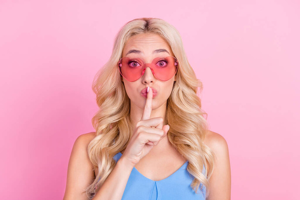 Fényképezés portré mosolygós nő visel napszemüveg tartása titkos ujját ajkak közelében elszigetelt pasztell rózsaszín szín háttér. - Fotó, kép