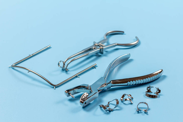 Perforación de orificios dentales, abrazaderas metálicas, un marco metálico y un fórceps de goma en el fondo azul. Concepto de herramientas médicas. - Foto, Imagen