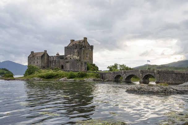 View of Eilean Donan Castle, Scotland, United Kingdom with a river and stone bridge on a cloudy day - Fotoğraf, Görsel
