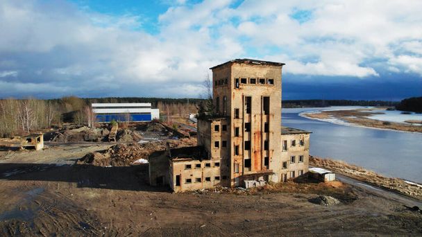Old tall ruined building, drone shot, camera flying around building, there is small river nearby, lot of clouds in sky - Фото, зображення