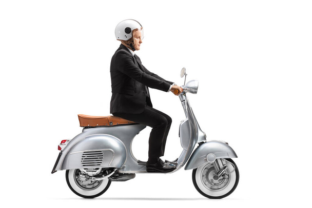 Mature businessman with a helmet riding a vintage scooter isolated on white background - 写真・画像