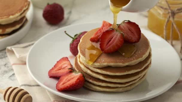 Verter jarabe o miel en panqueques americanos decorados con fresas. Desayuno sabroso y saludable - Imágenes, Vídeo