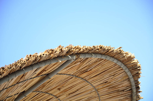 A straw beach umbrella under a blue sky - 写真・画像