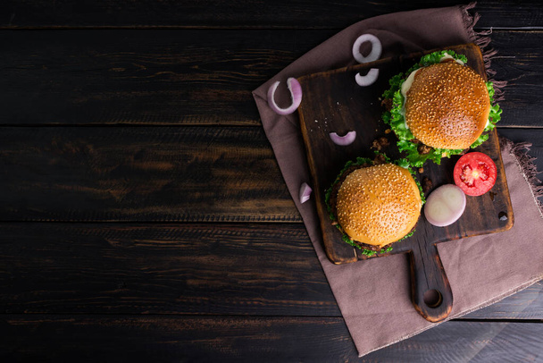 おいしい自家製バーガーは黒い木製のテーブルに設定されています。おいしい焼きたての鶏、豚肉、または牛肉のハンバーガー-トップビュー - 写真・画像
