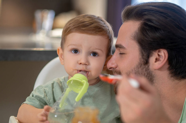 Eating. Cute little boy drinking from his bottle while dad feeding him - Fotó, kép