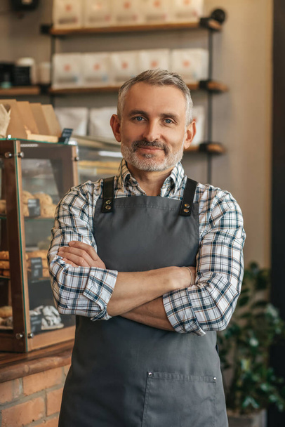Professional. Confident middle aged man in apron folded hands on chest looking at camera standing in his cafe - Foto, afbeelding
