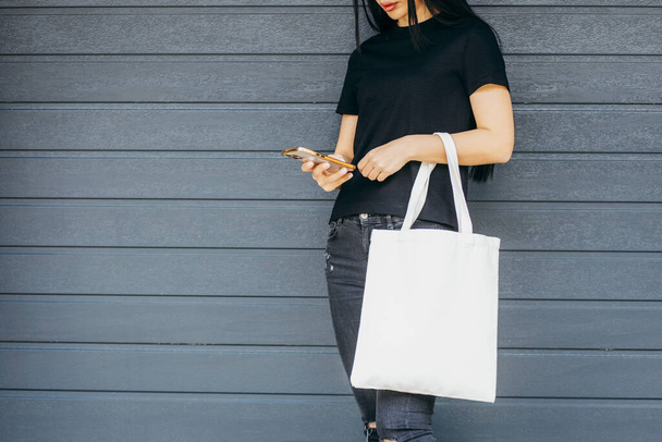 Jovem modelo menina na rua segurando branco eco saco e telefone celular, zombar - Foto, Imagem