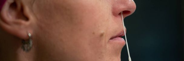 Крупный план женщины, берущей образец носа с ватным тампоном для домашнего теста коронавируса. Широкий обзор изображения. - Фото, изображение