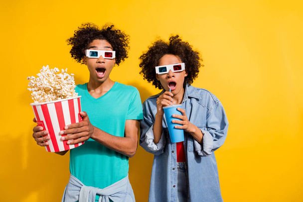 Photo of shocked afro american people couple wear 3d glasses movie pop corn fly drink isolated on yellow color background. - Zdjęcie, obraz