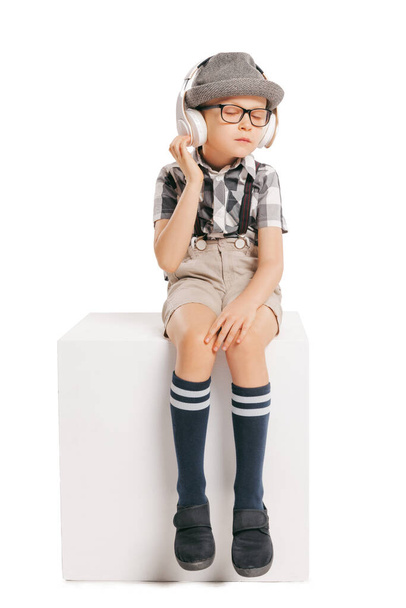 Music. Portrait of cute little boy, happy kid in eyeglasses and hat isolated on white studio background with copyspace for ad. Concept of child emotions, facial expression, beauty and ad. - Photo, Image