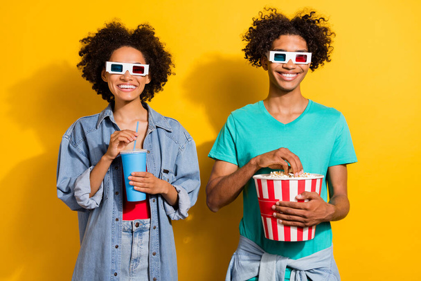 Photo of cheerful afro american people couple movie glasses eat pop corn drink isolated on yellow color background. - Фото, зображення