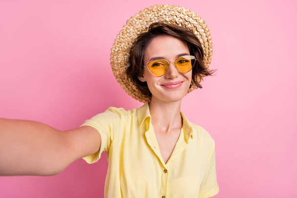 Photo of cute young brunette lady do selfie wear yellow t-shirt cap eyewear isolated on pink color background. - Foto, afbeelding