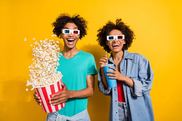 Photo of amazed happy dark skin people couple film glasses pop corn fly drink isolated on yellow color background. - Foto, Imagen