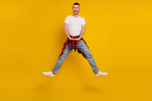 Full size photo of amazed man wear plaid shirt on waist jump up sale isolated on yellow color background. - 写真・画像