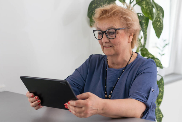 Seniorin telefoniert zu Hause vom Tablet-Computer aus. - Foto, Bild