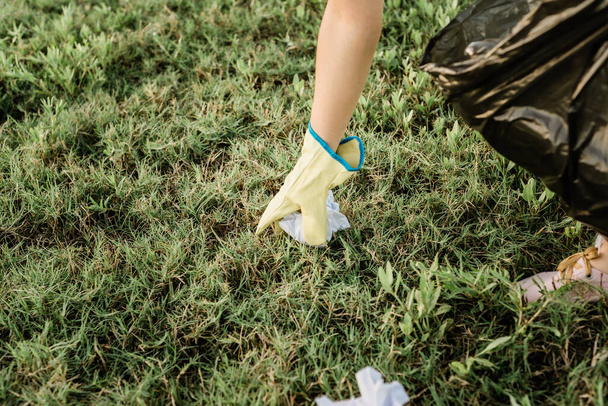 A closeup of a person's hand wearing rubber gloves and picking up trash from the vibrant green grass - Photo, Image
