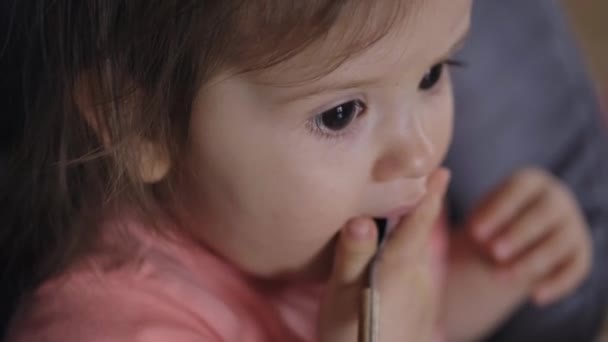 Cute baby girl biting a spoon while sitting on high-chair. Healthy food. Beautiful closeup portrait. Beautiful young girl. - Footage, Video
