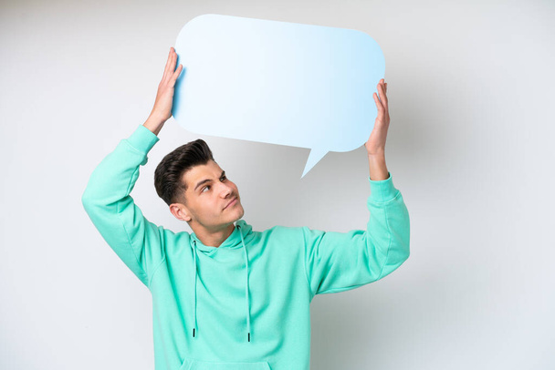 Young handsome caucasian man isolated on white bakcground holding an empty speech bubble and with sad expression - Foto, imagen