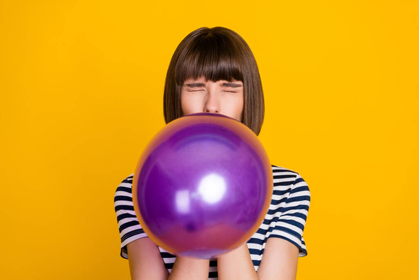 Photo of impressed brunette millennial lady blow balloon closed eyes wear blue t-shirt isolated on yellow background. - Photo, Image