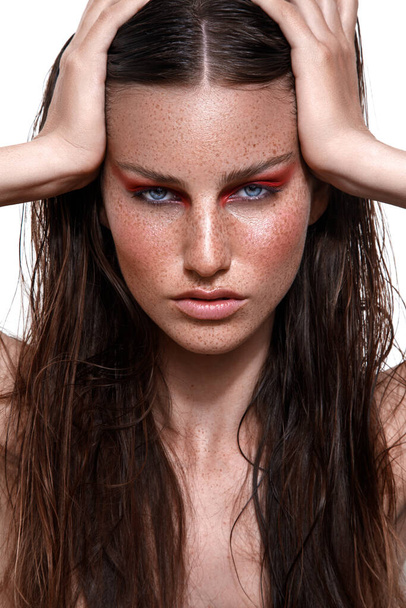 A studio shot of Caucasian woman with brunette hair and freckles on face posing with hands on head - Foto, imagen