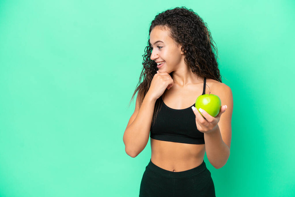 Young Arab woman with an apple isolated on green background thinking an idea and looking side - Foto, Imagem