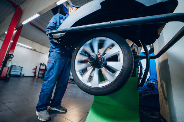 Auto mechanic uses tire balancing machine and turning tire - Photo, Image