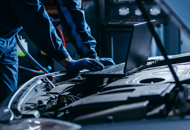 Close up hands of auto electrician using a computer laptop to diagnosing and checking up on car engines parts for fixing and repair - Photo, Image