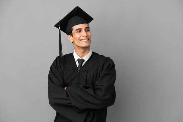Young Argentinian university graduate isolated on grey background with arms crossed and happy - Photo, Image