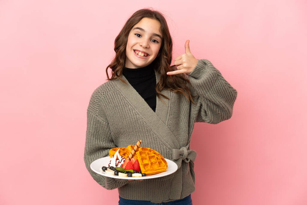 Little girl holding waffles isolated on pink background making phone gesture. Call me back sign - Fotó, kép