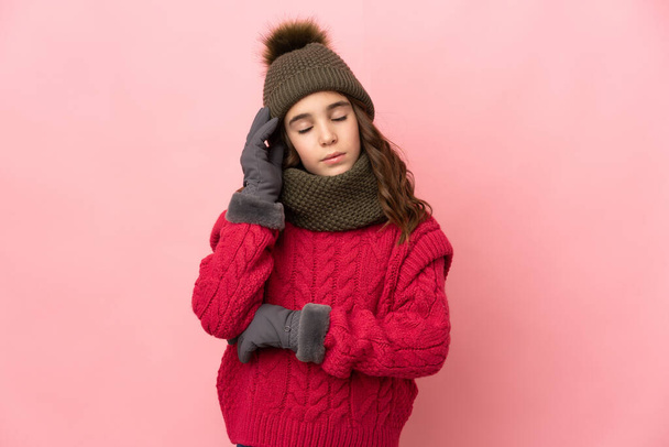Маленька дівчинка з зимовим капелюхом ізольована на рожевому фоні з головним болем
 - Фото, зображення