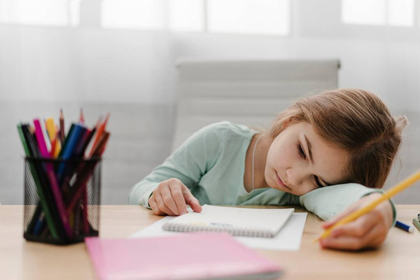niña aburrida tomando notas mientras tiene clase en línea. Foto de alta resolución - Foto, imagen