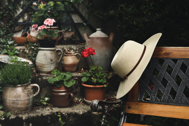 Women's summer hat on a wooden bench in the garden, calm lifestyle and cottagecore concept - Fotó, kép