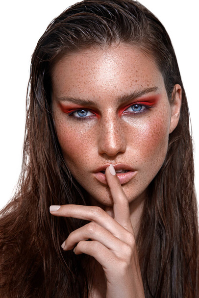 A studio shot of Caucasian woman with brunette hair and freckles on face posing with finger on lips - Fotografie, Obrázek