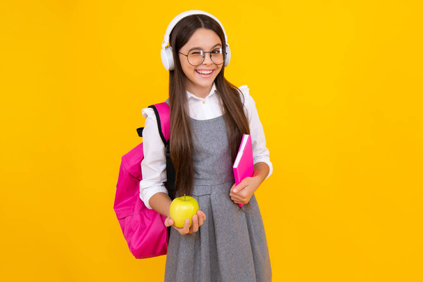 Schulkind, Schülerin im Teenageralter mit Rucksack halten Apfel und Buch isoliert auf gelb. Glückliches Gesicht, positive und lächelnde Emotionen des Teenie-Mädchens - Foto, Bild