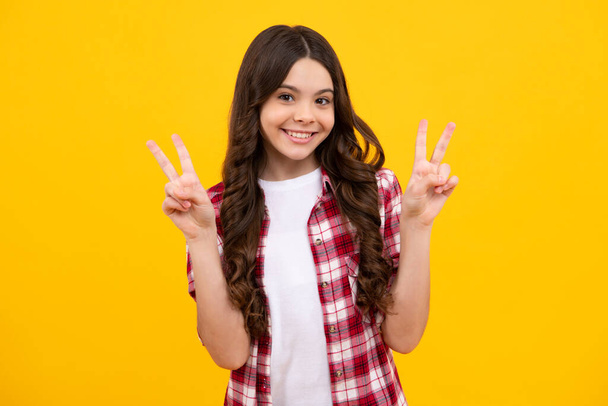 Egy tinédzser kislány áll az elszigetelt sárga háttér felett, és mutatja, hogy az ujjai győzelmet jeleznek. Kettő: V-jel. Boldog tinédzser, pozitív és mosolygós érzelmek tini lány - Fotó, kép