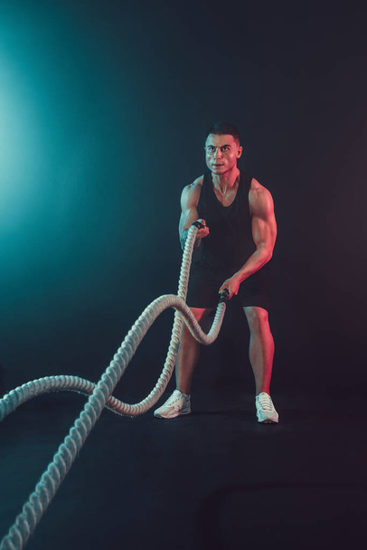 Athletic looking bodybulder work out with battle rope on dark studio background with smoke. Strength and motivation.  - Foto, Imagem