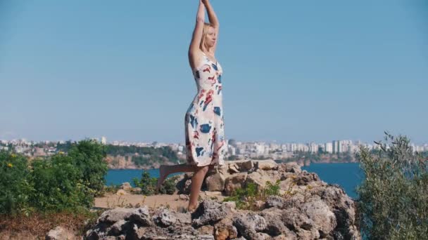 Die erwachsene blonde Frau steht auf dem Felsen und macht Atemübungen in der Ferne von der Stadt. Mittelschuss - Filmmaterial, Video