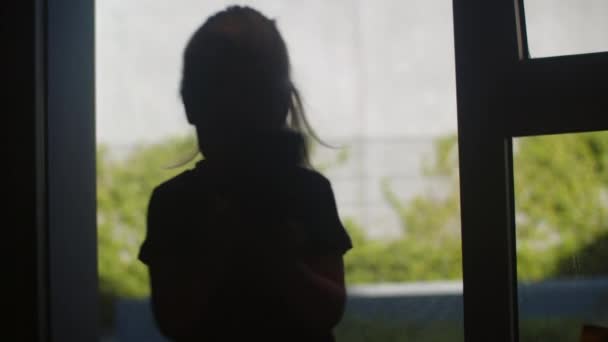 Mała dziewczynka obraca się podczas rozmowy wideo na smartfonie, widok na okno. Zabawny i aktywny dzieciak rozmawiający przez telefon - Materiał filmowy, wideo