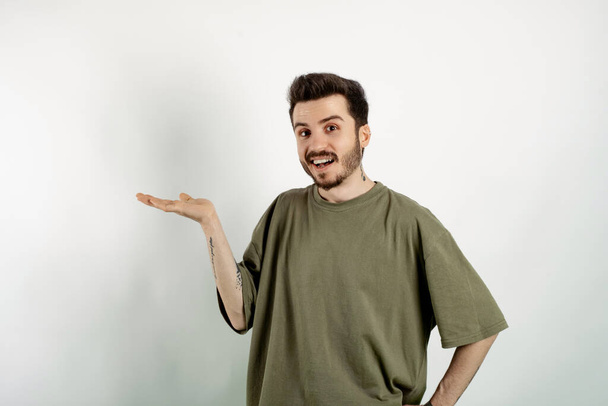 Handsome caucasian man wearing khaki t-shirt posing isolated over white background smiling cheerfully, feeling happy and showing a concept in copy space with palm of hand - Foto, Bild