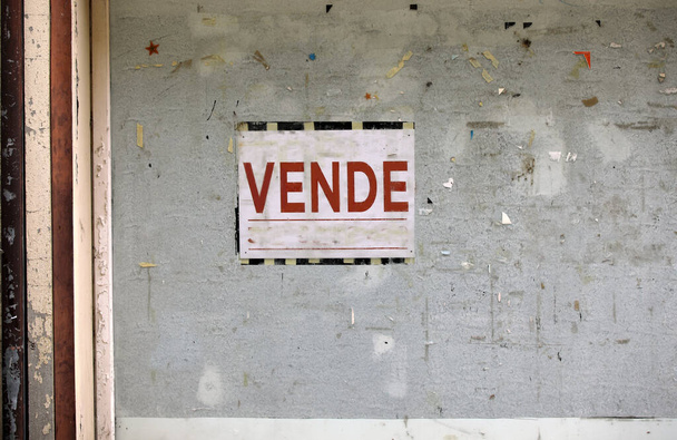 a válság miatt bezárt üzlethelyiség ablaka és a VENDE szöveggel ellátott nagy tábla, amely olaszul eladó - Fotó, kép
