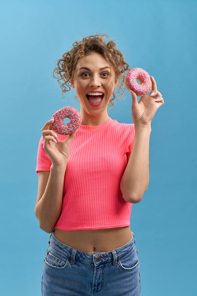Funny girl with donuts in hands, laughing, looking at camera in studio. Portrait view of pretty woman holding doughnuts, having fun, isolated on cyan background, with copy space. Concept of happiness. - Fotó, kép