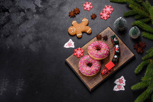 ピンク色の釉薬と色のついた美しいドーナツは、暗いコンクリートの背景に振りかけます。クリスマステーブルへのお菓子 - 写真・画像
