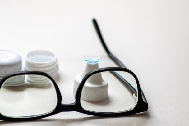 Blue contact lens through black eyeglasses shows different eyewear to correct farsightedness and nearsightedness by optometry or eye doctor against myopia with visual eye correction for perfect vision - Foto, afbeelding