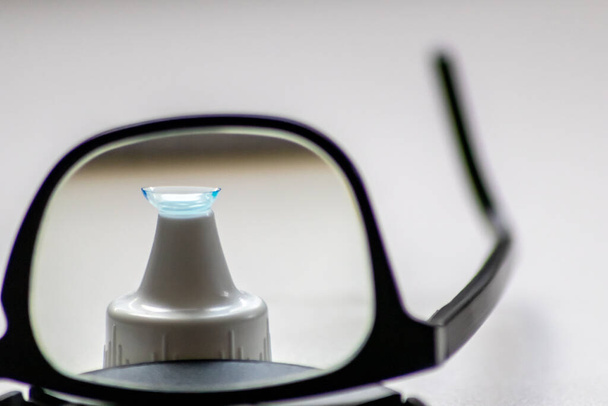 黒眼鏡を通してブルーコンタクトレンズは、完璧なビジョンのための視覚的な目の補正と近視に対する近視や近視の光医師を修正するために別の目を示しています - 写真・画像