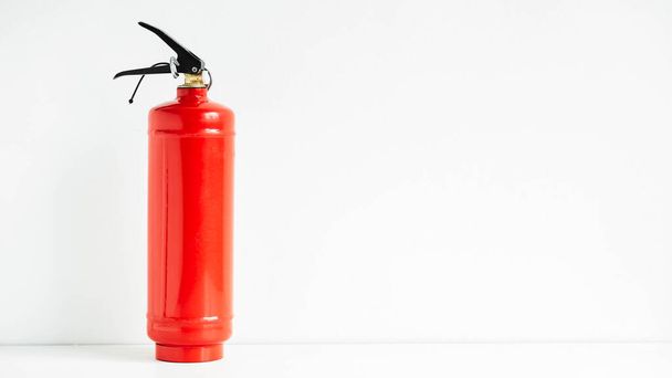 Red fire extinguisher on a white wall background. - Foto, afbeelding