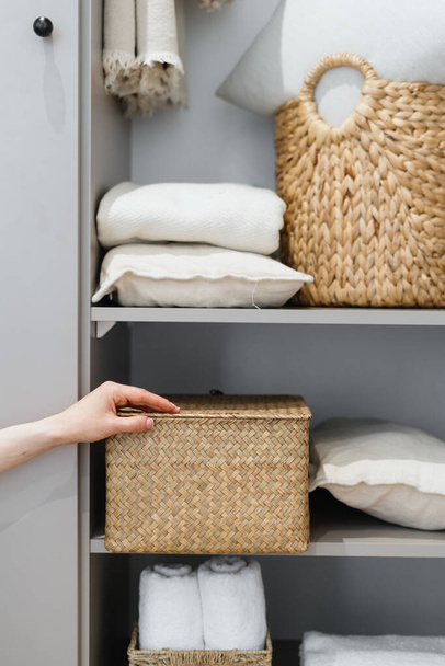 Przycięty widok schludnej gospodyni domowej stawia wiklinowe pudełko z ubraniami na szafie, podczas ogólnego czyszczenia przez nowoczesny system przechowywania. Koncepcja komfortowej organizacji miejsca w mieszkaniu - Zdjęcie, obraz